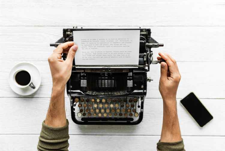 person holding white paper and typewriter